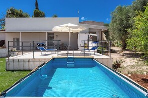 A swimming pool with a sunshade, lounge chairs, and a patio area.