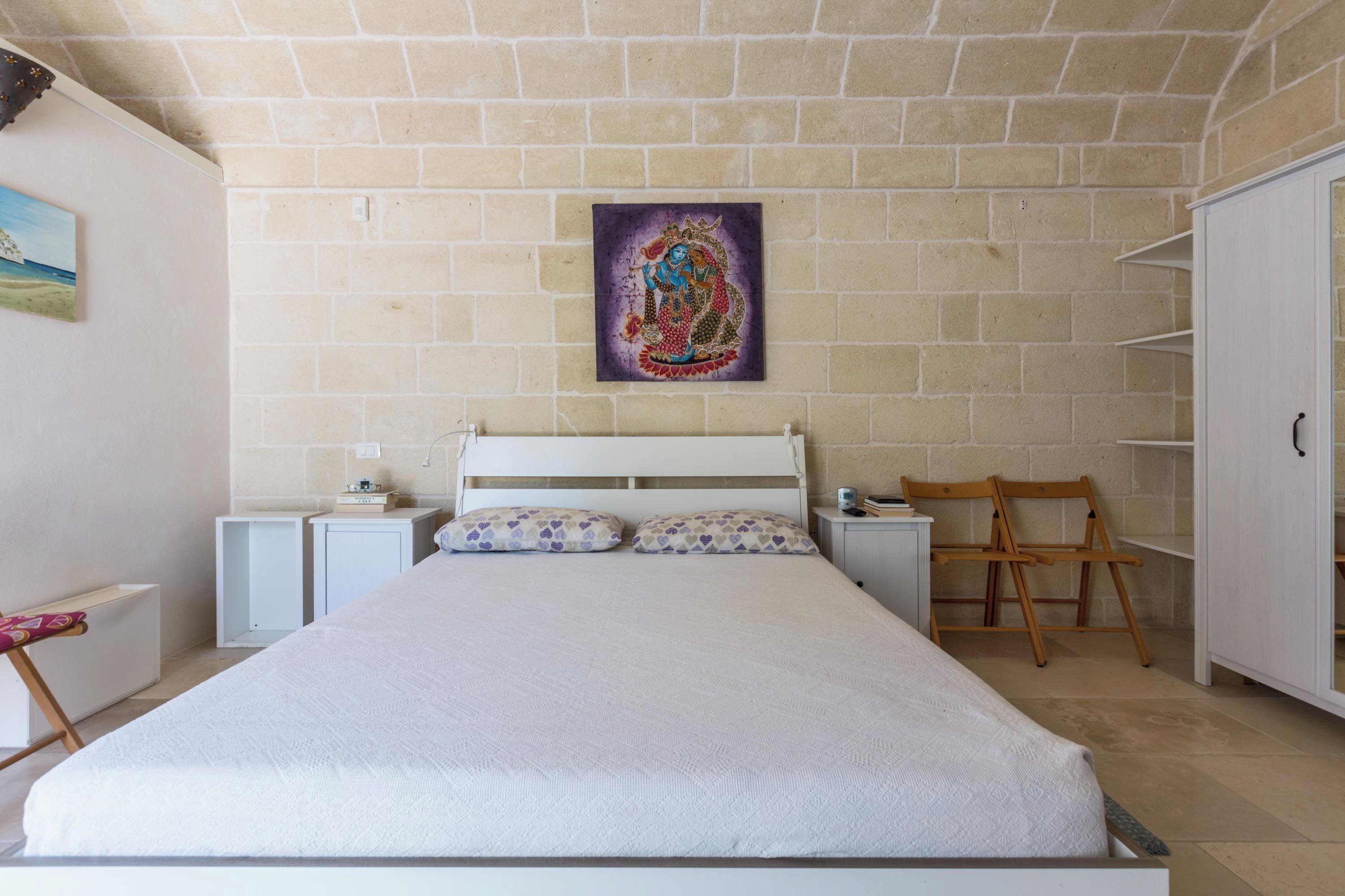 A bedroom with a large bed, a nightstand, a chair, and a wardrobe.