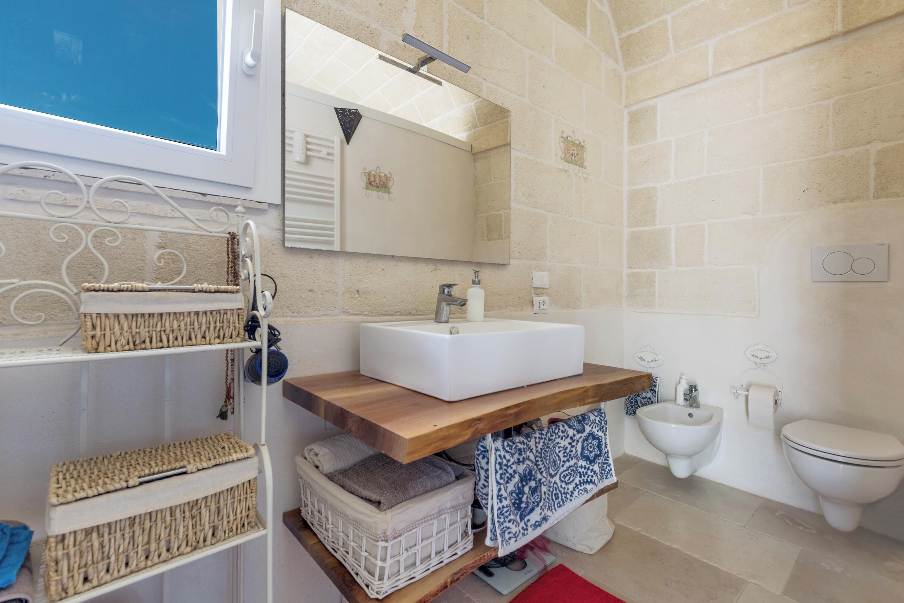 A bathroom with a white sink, wooden vanity, wicker baskets, a bidet, and a toilet.