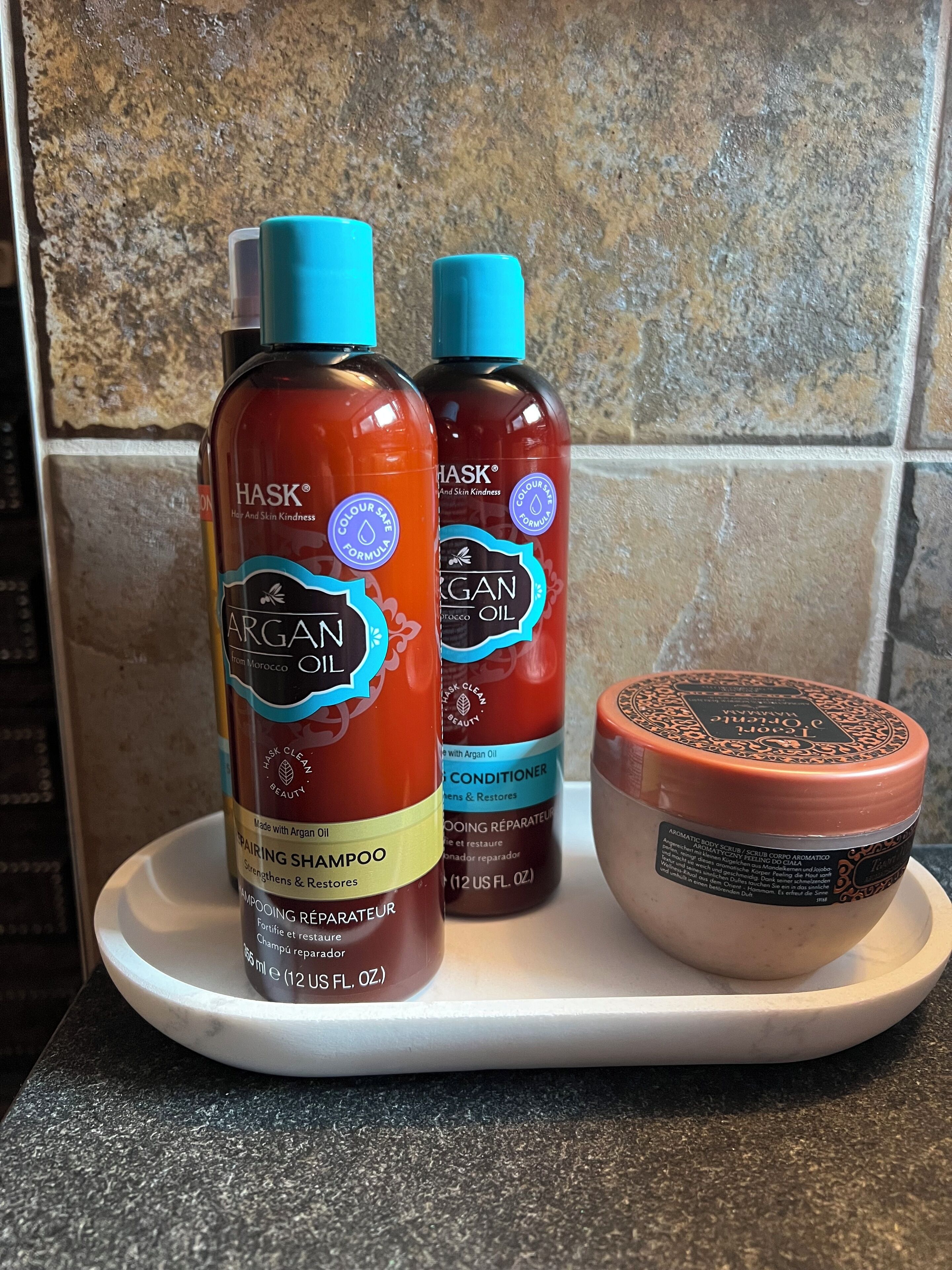Two bottles of Argan oil-based shampoo and conditioner, and a container of body scrub on a white tray.