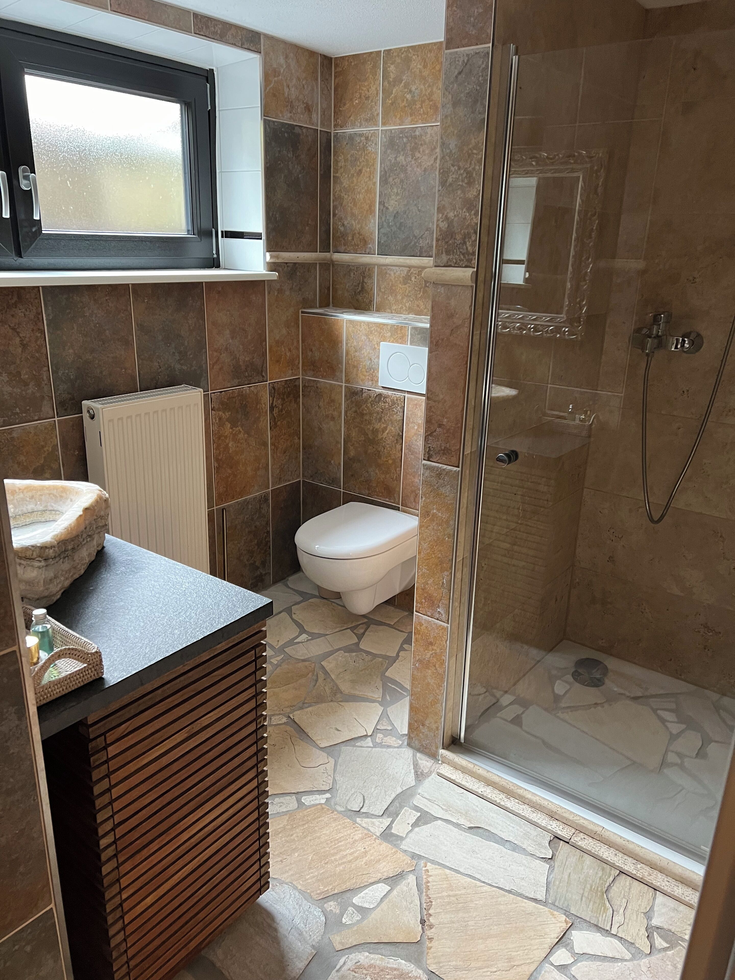 Une salle de bain avec un sol en pierre, des toilettes, une douche et un lavabo doté d’un receveur en pierre.