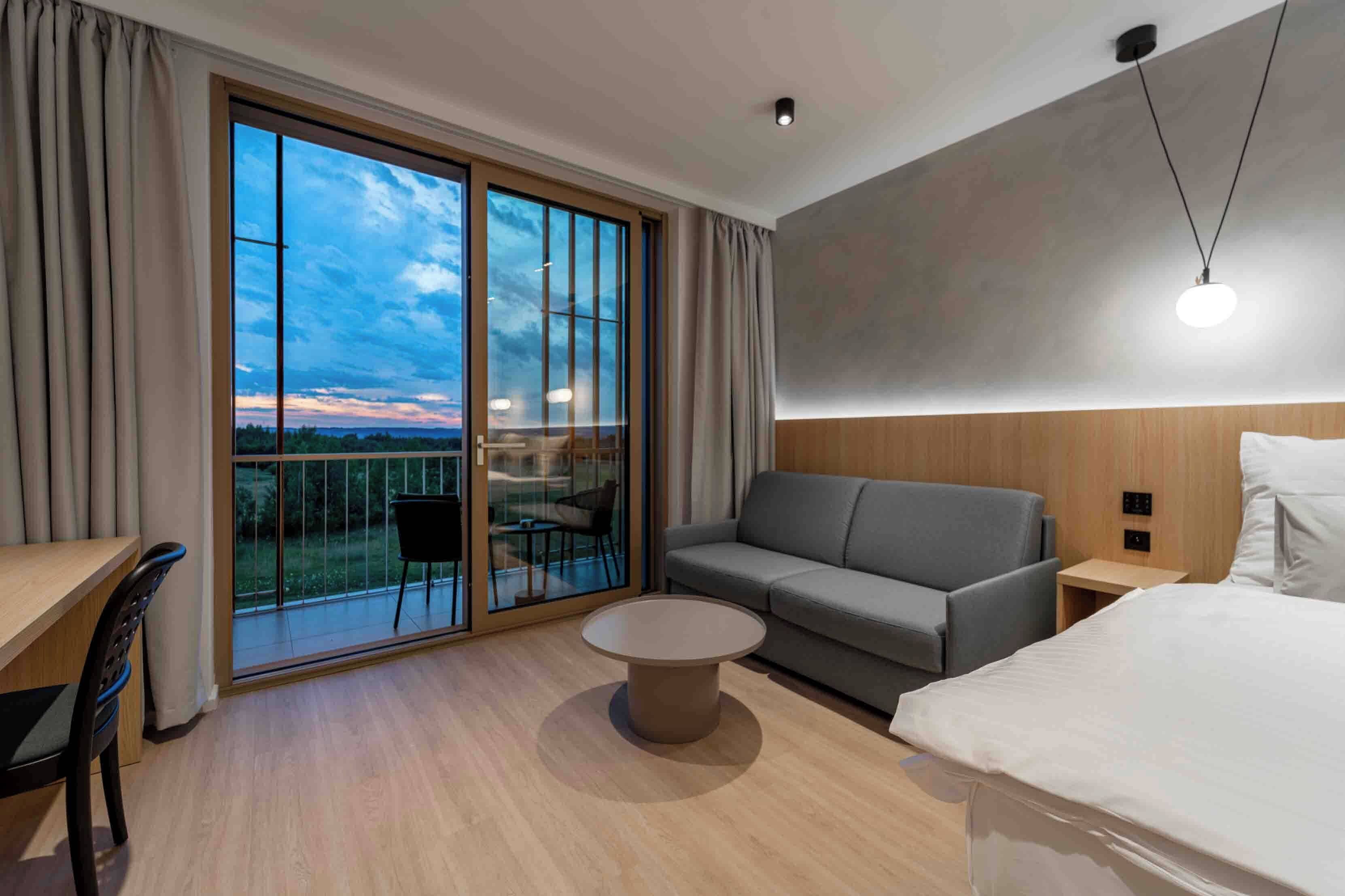 A hotel room with a balcony, a sofa, a bed, a desk, and a round coffee table.