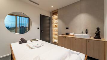 Een moderne slaapkamer met een groot bed, een ronde spiegel, een ingebouwde wastafel en uitzicht op de omgeving door een raam.