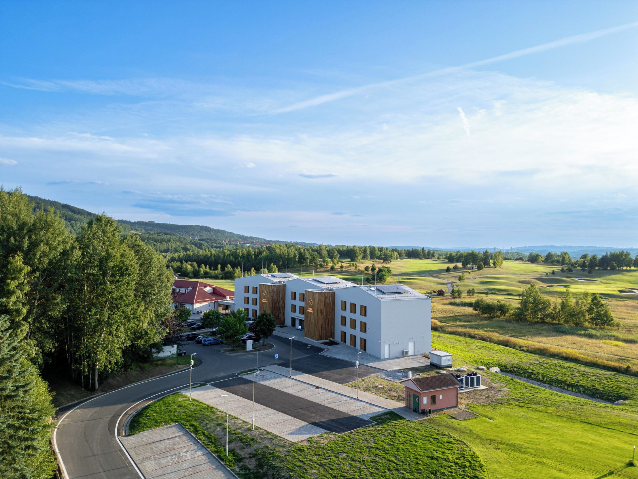 A modern building complex with a parking area and a view of a green landscape.