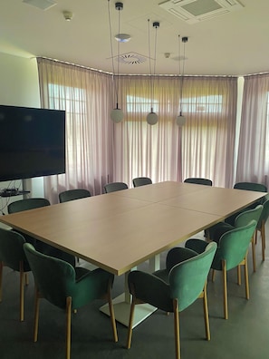 Conference room with a large table and eight chairs, featuring a flat-screen TV and natural light.