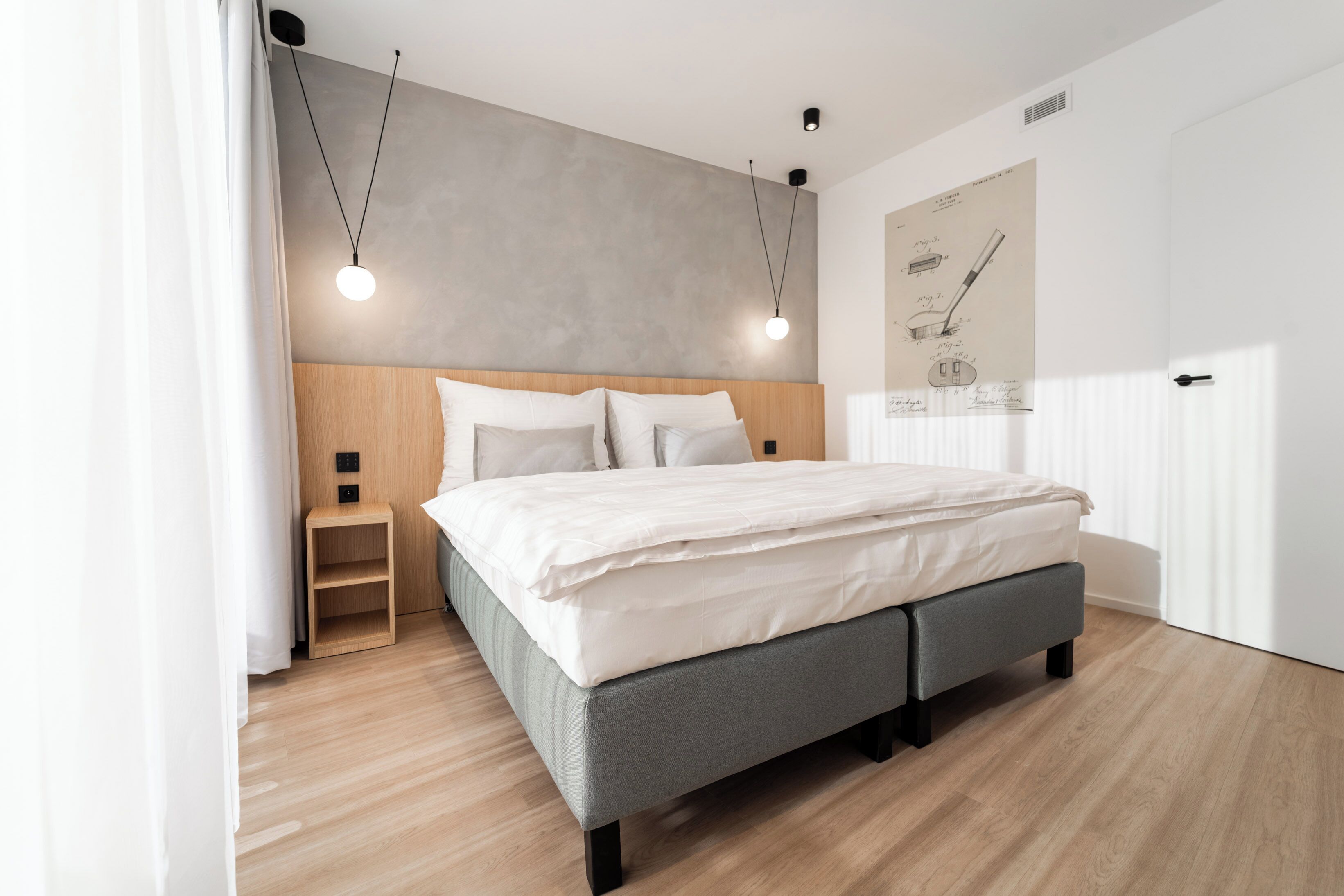 Un dormitorio moderno con cabecera de madera, cama tapizada de gris, mesita de noche de madera y lámparas colgantes.