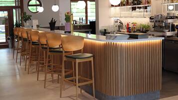 A modern bar area with wooden bar stools, a counter with a built-in wine cooler, and a variety of bar tools and bottles.