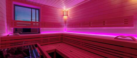 Een sauna met houten banken en een raam, verlicht met roze verlichting.