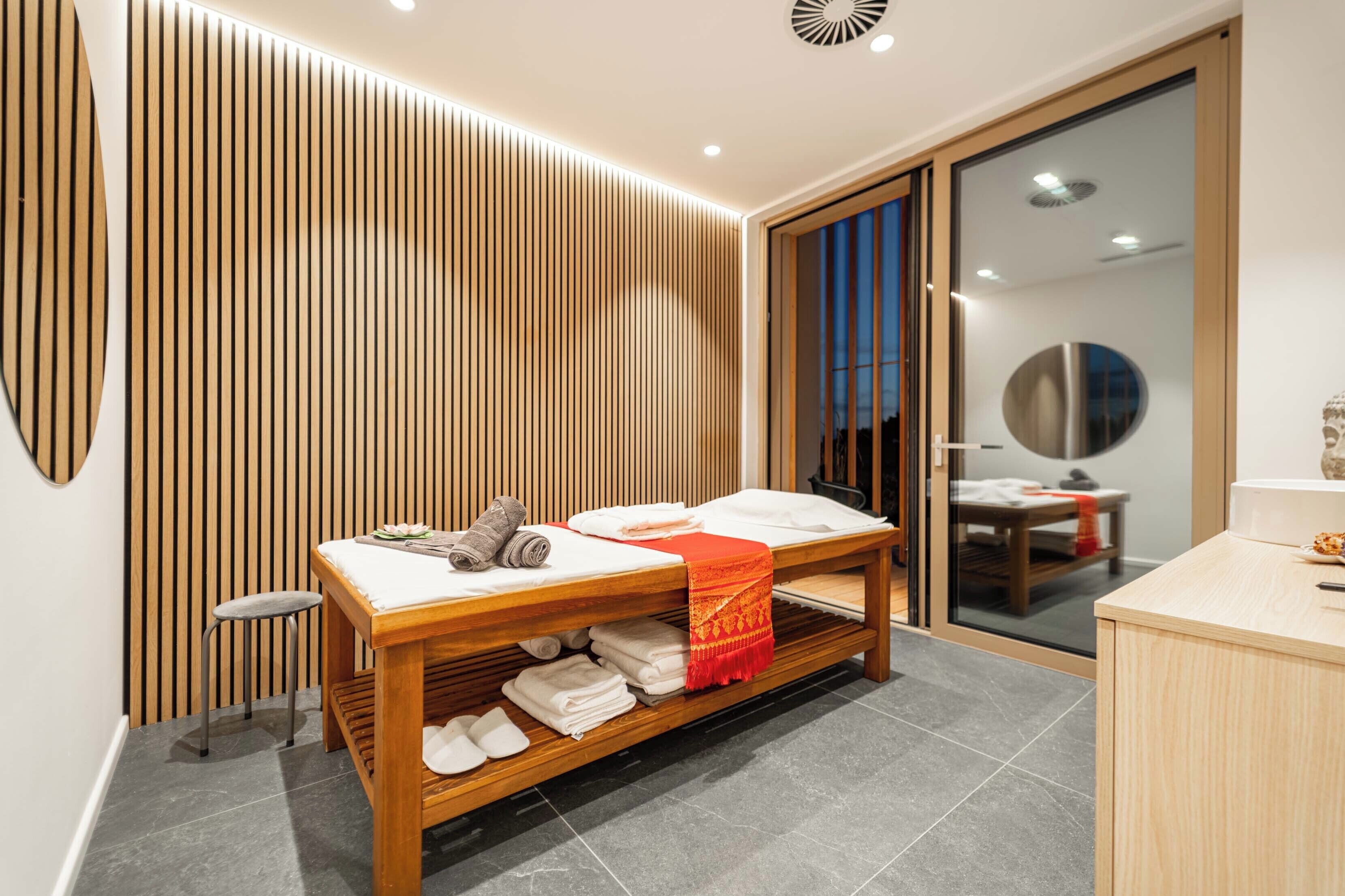 Un moderno cuarto de spa con una camilla de madera, un taburete pequeño y un armario de madera.