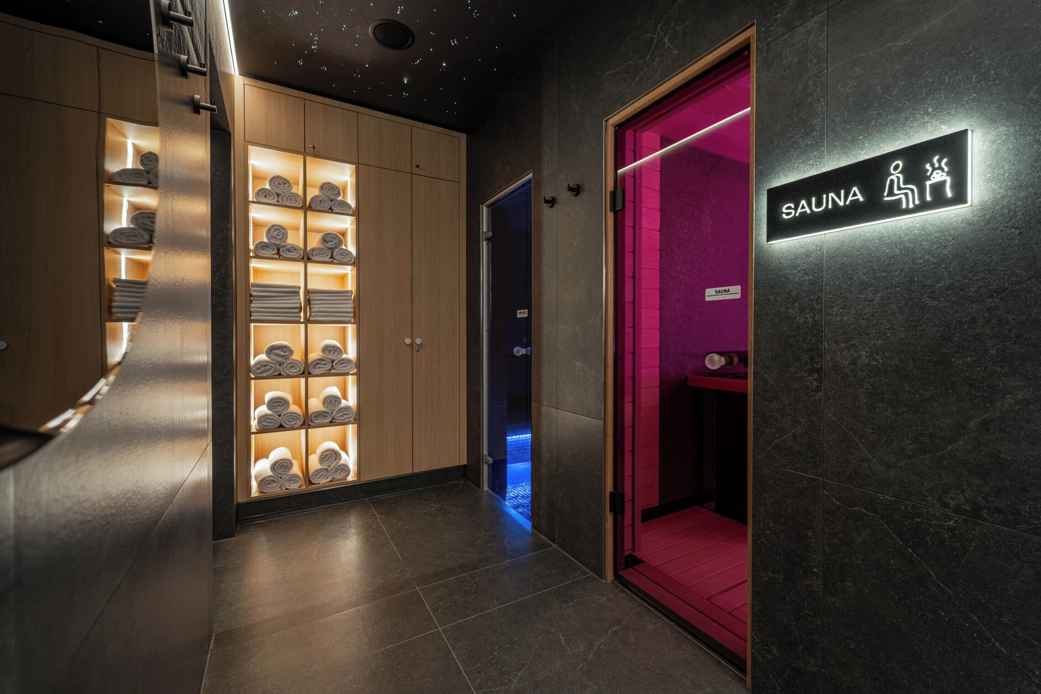 A modern spa area with a sauna sign, wooden shelves with towels, and a red carpet leading to the sauna.