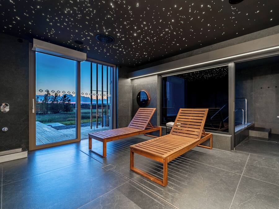 Um interior moderno com duas poltronas de madeira, uma grande porta de correr de vidro que dá para um deck e um teto com luzes que lembram estrelas.