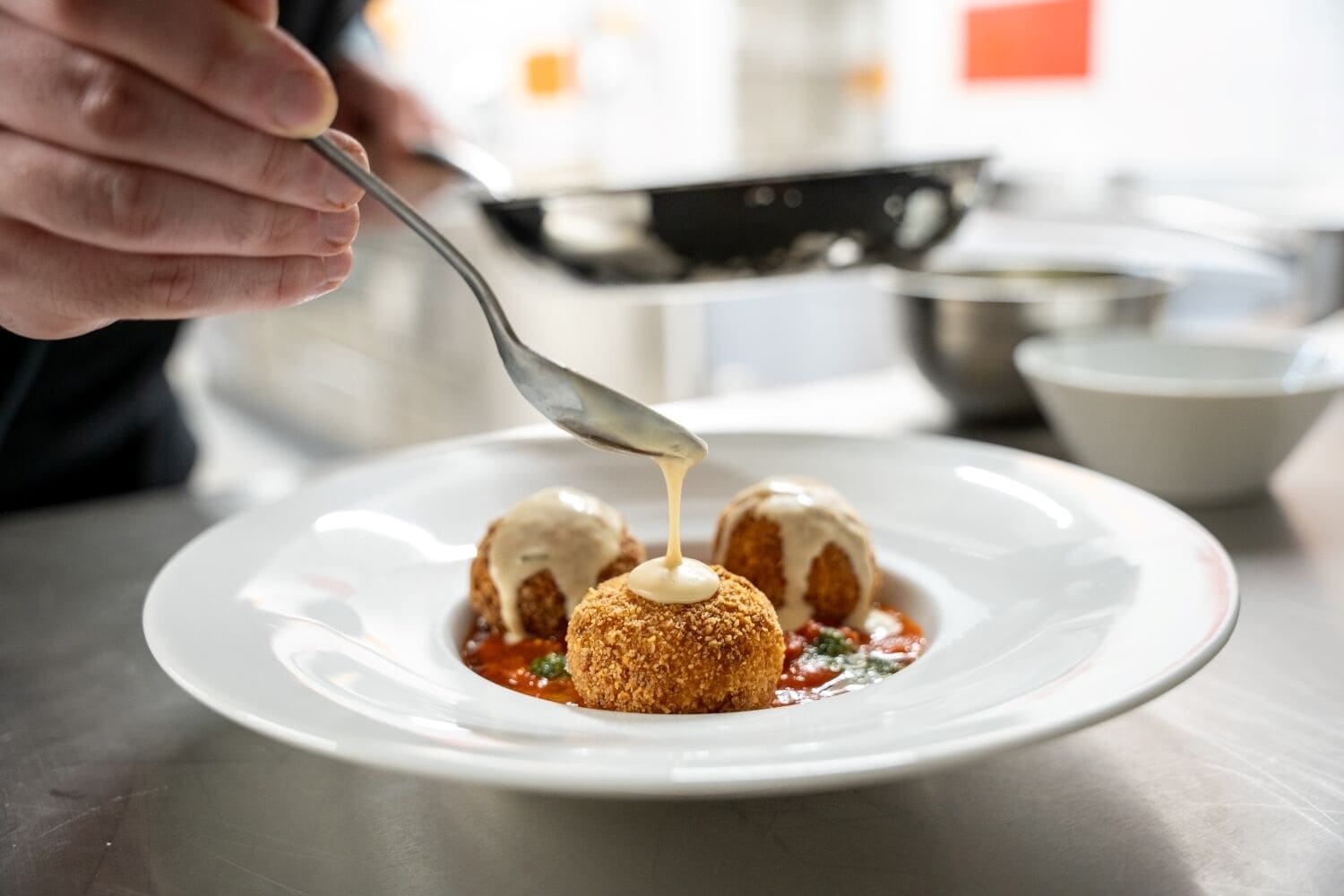 Een bord met drie gepaneerde balletjes en saus die erover gegoten wordt.