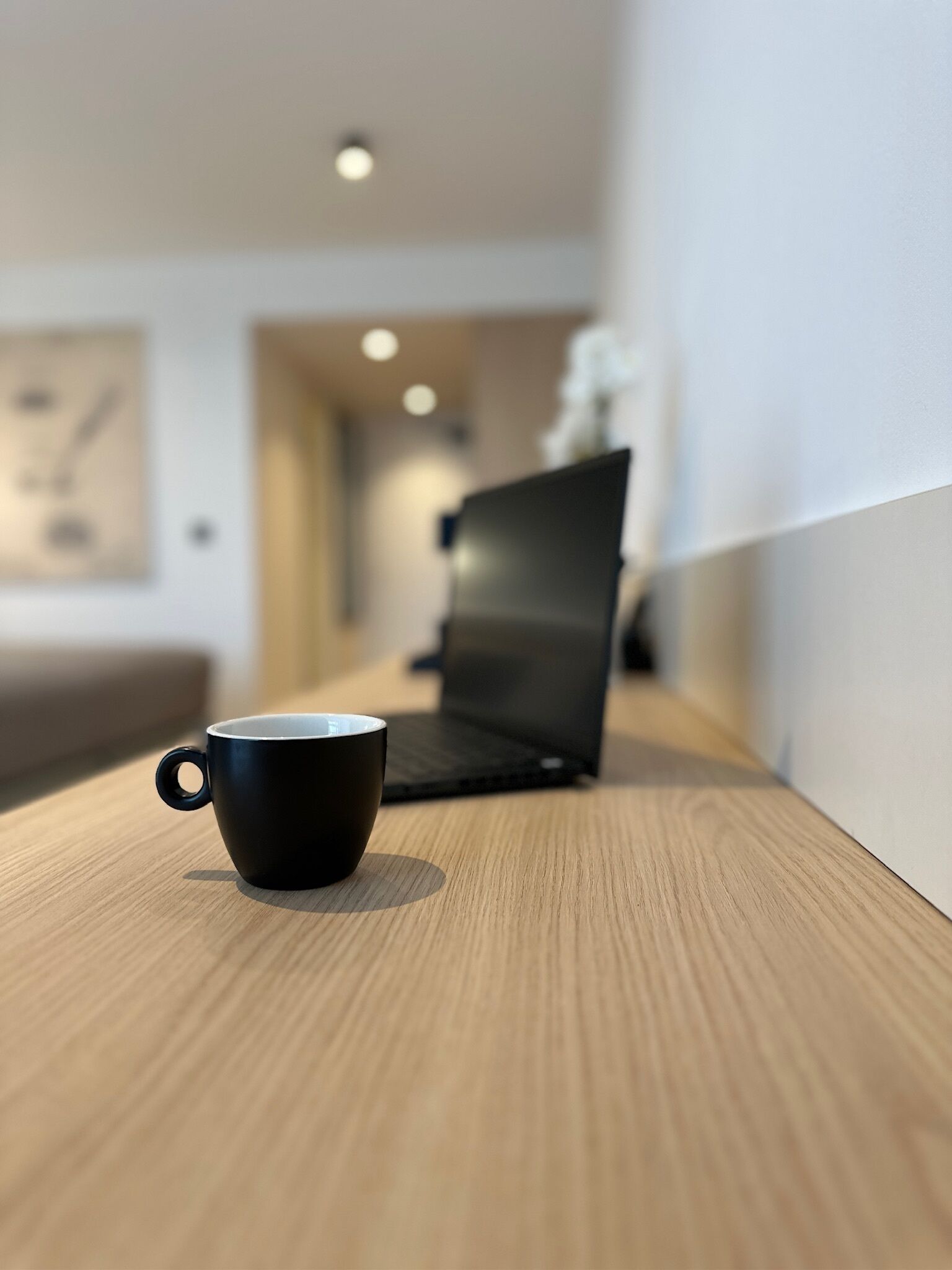 Una taza negra sobre una superficie de madera, con una computadora portátil al fondo.