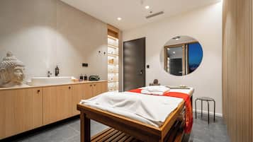 A modern bathroom with a wooden vanity, a large mirror, and a bed with a red bedspread.
