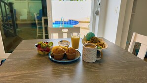 Una mesa de desayuno con un frutero, muffins, un vaso de jugo de naranja y una taza.