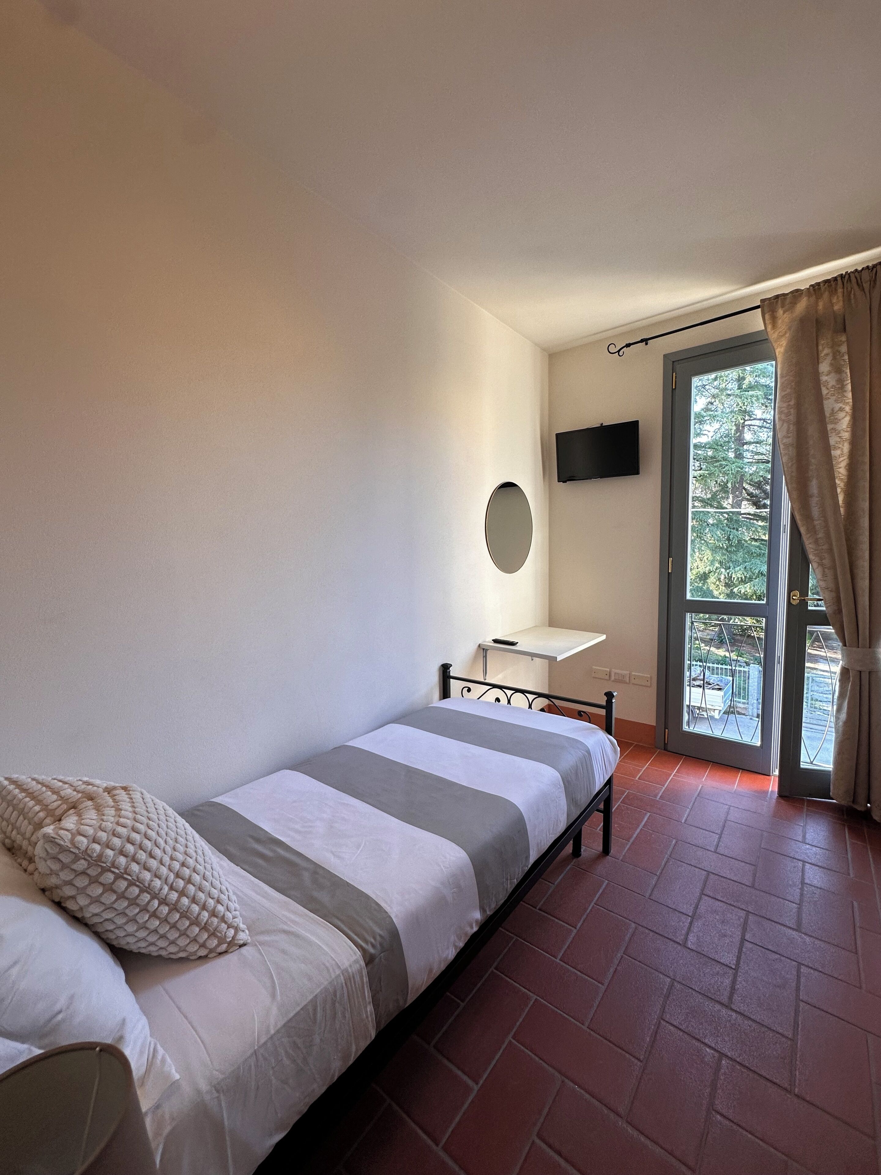 A bedroom with a bed, a desk, a TV, and a window with curtains.