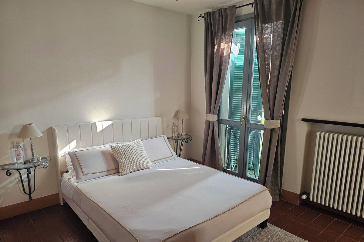 A neatly arranged bedroom with a bed, bedside tables, a radiator, and a window with curtains.