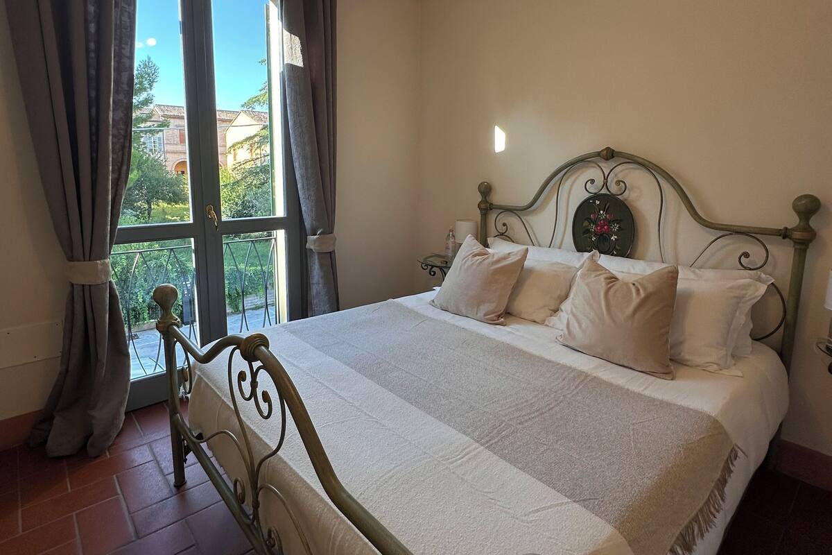 A bedroom with a bed, curtains, a ceiling fan, and a window with a view of buildings outside.