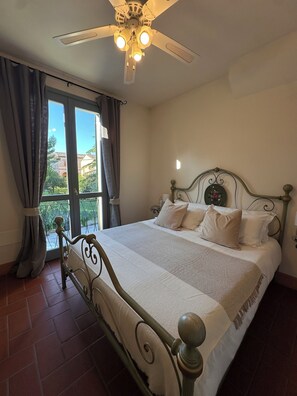 A bedroom with a bed, curtains, a ceiling fan, and a window with a view of buildings outside. - Casa Giulietta B&B (Santarcangelo di Romagna)