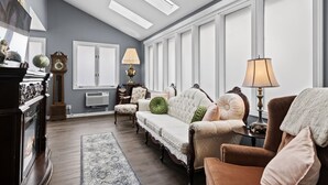 Ein Wohnzimmer mit Kamin, einer Couch, zwei Sesseln, einer Lampe, einer Uhr und einem Globus auf einem Kaminbrett.
