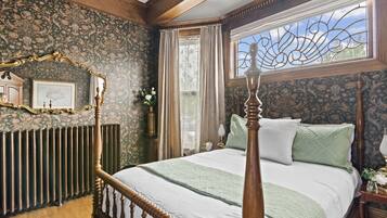 A bedroom with a four-poster bed, a radiator, a mirror, and a window with decorative ironwork.
