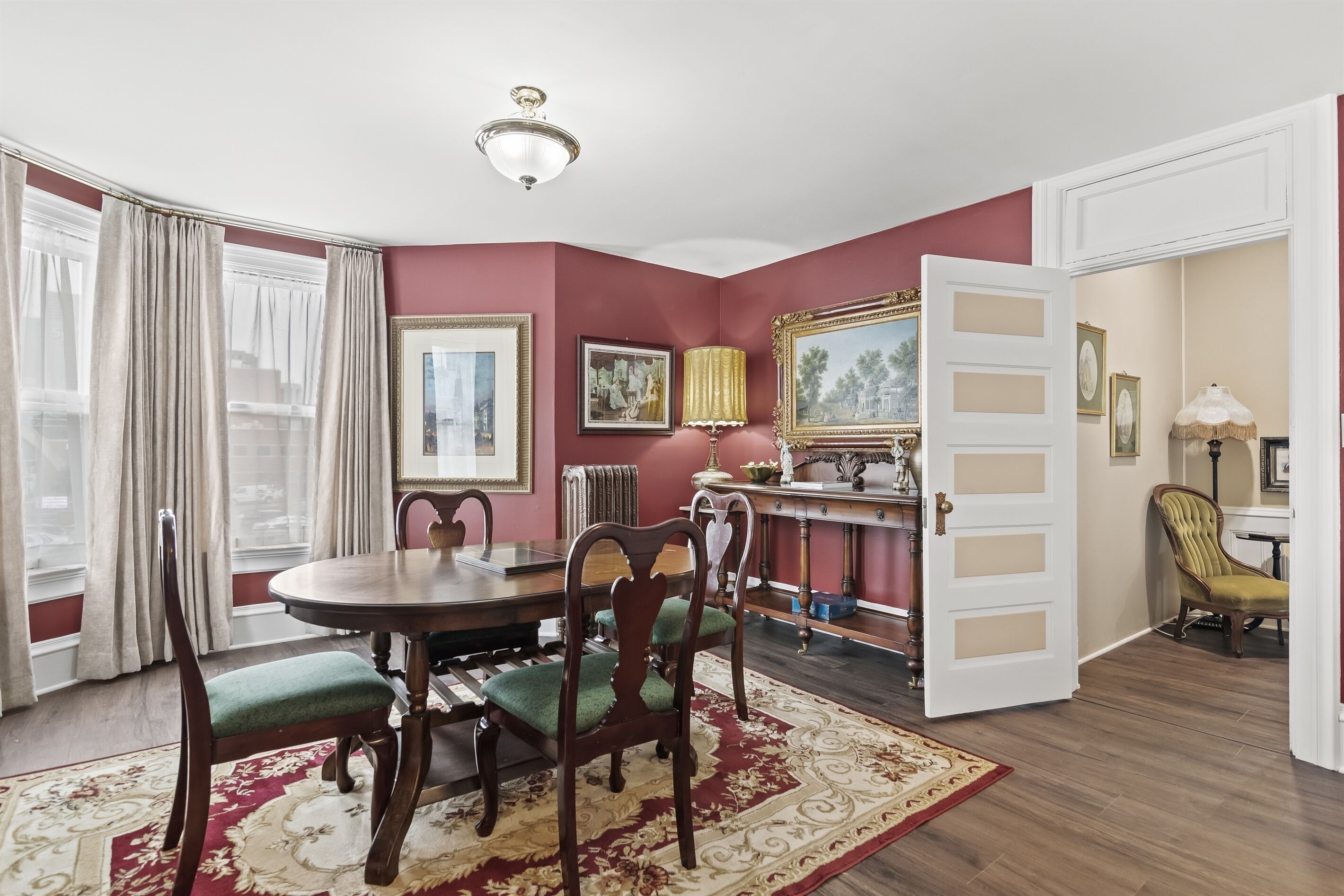 A dining room with a round table, chairs, a red carpet, and a chandelier.