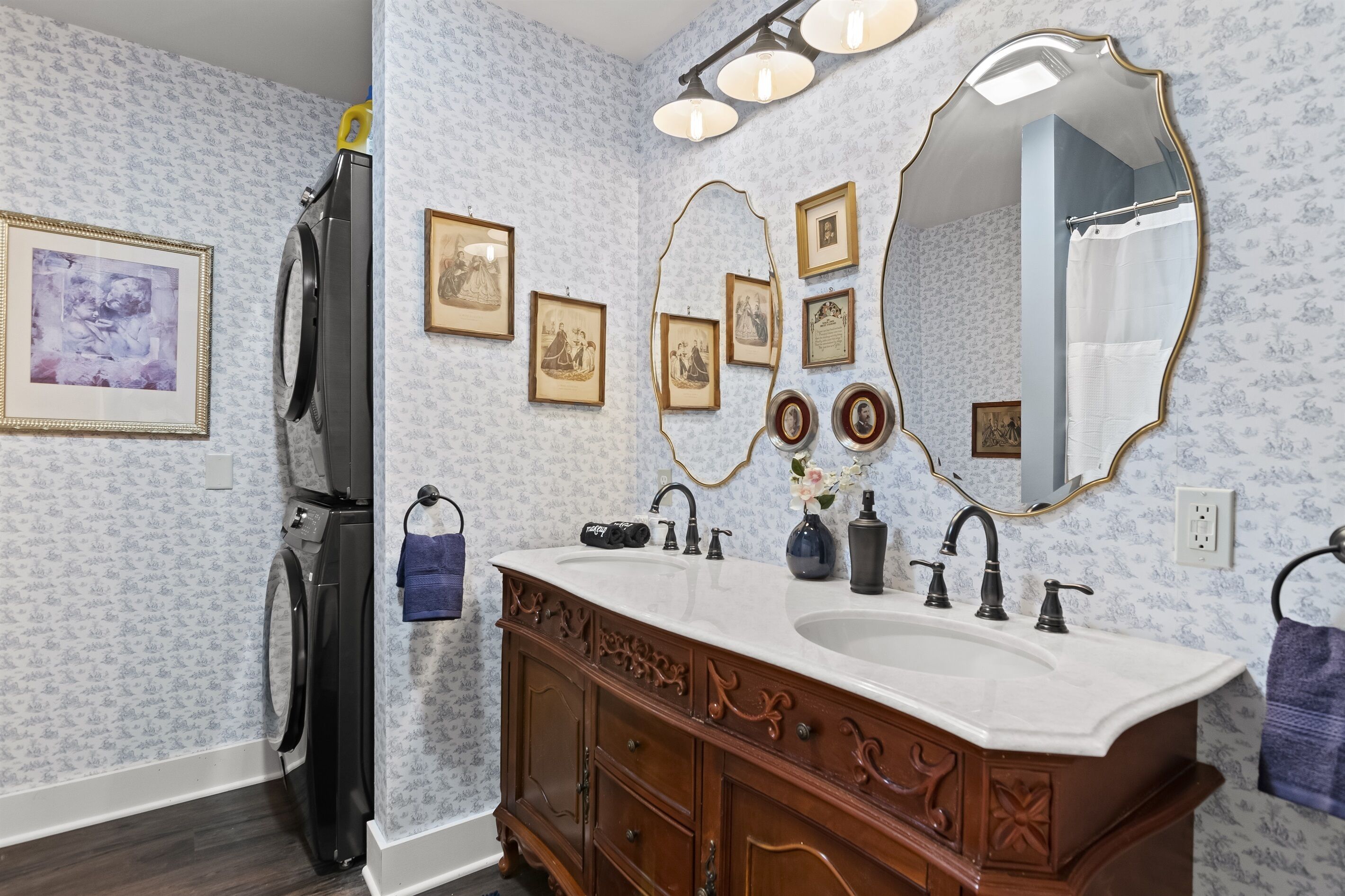 A bathroom with a double sink vanity, a large mirror, and wall-mounted framed pictures.