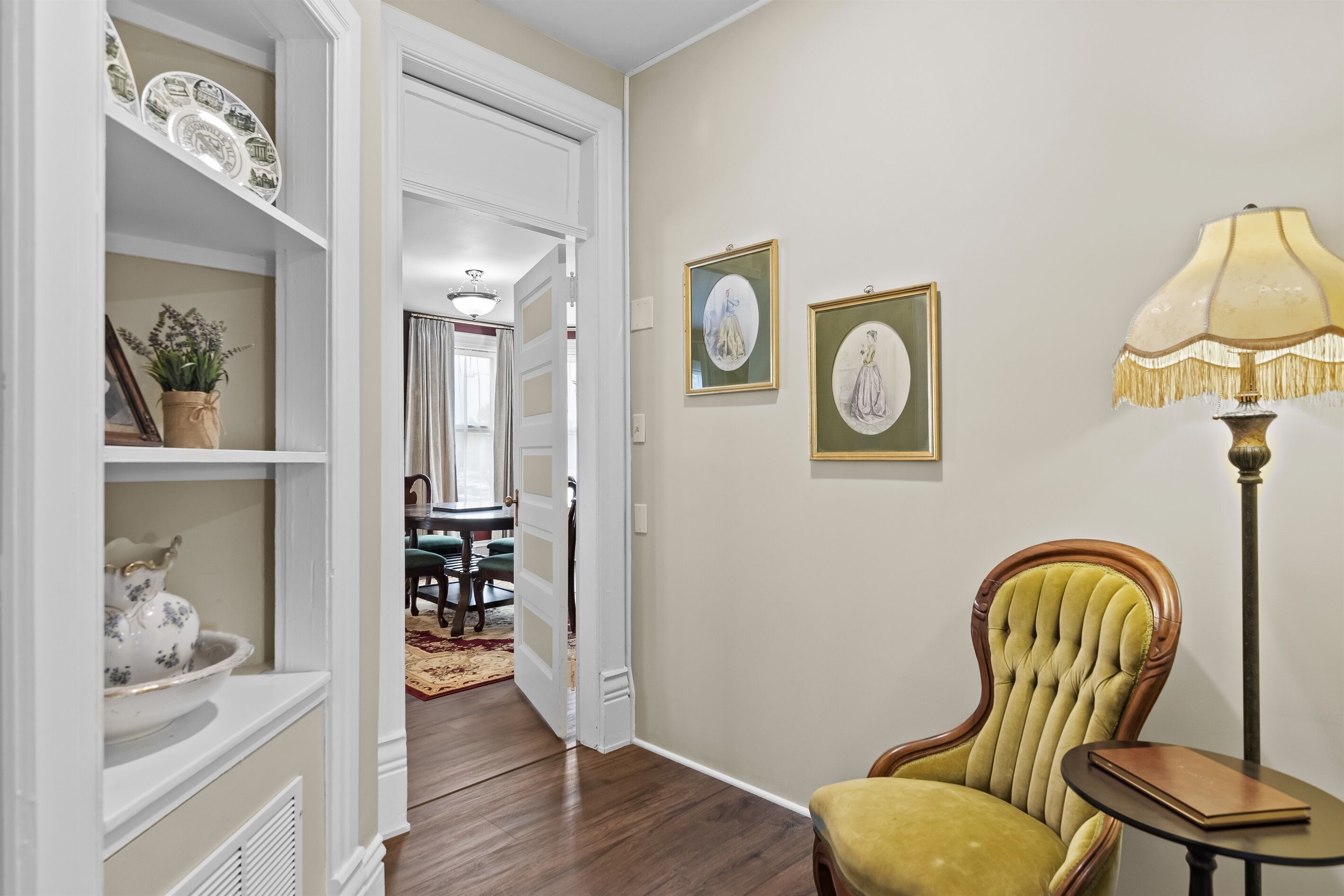 A hallway with a green armchair, a lamp, and framed pictures on the wall.