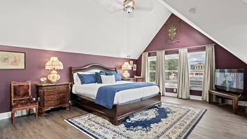 Een slaapkamer met een groot bed, een houten dressoir, een nachtkastje, een lamp, een televisie en uitzicht buiten door een raam.