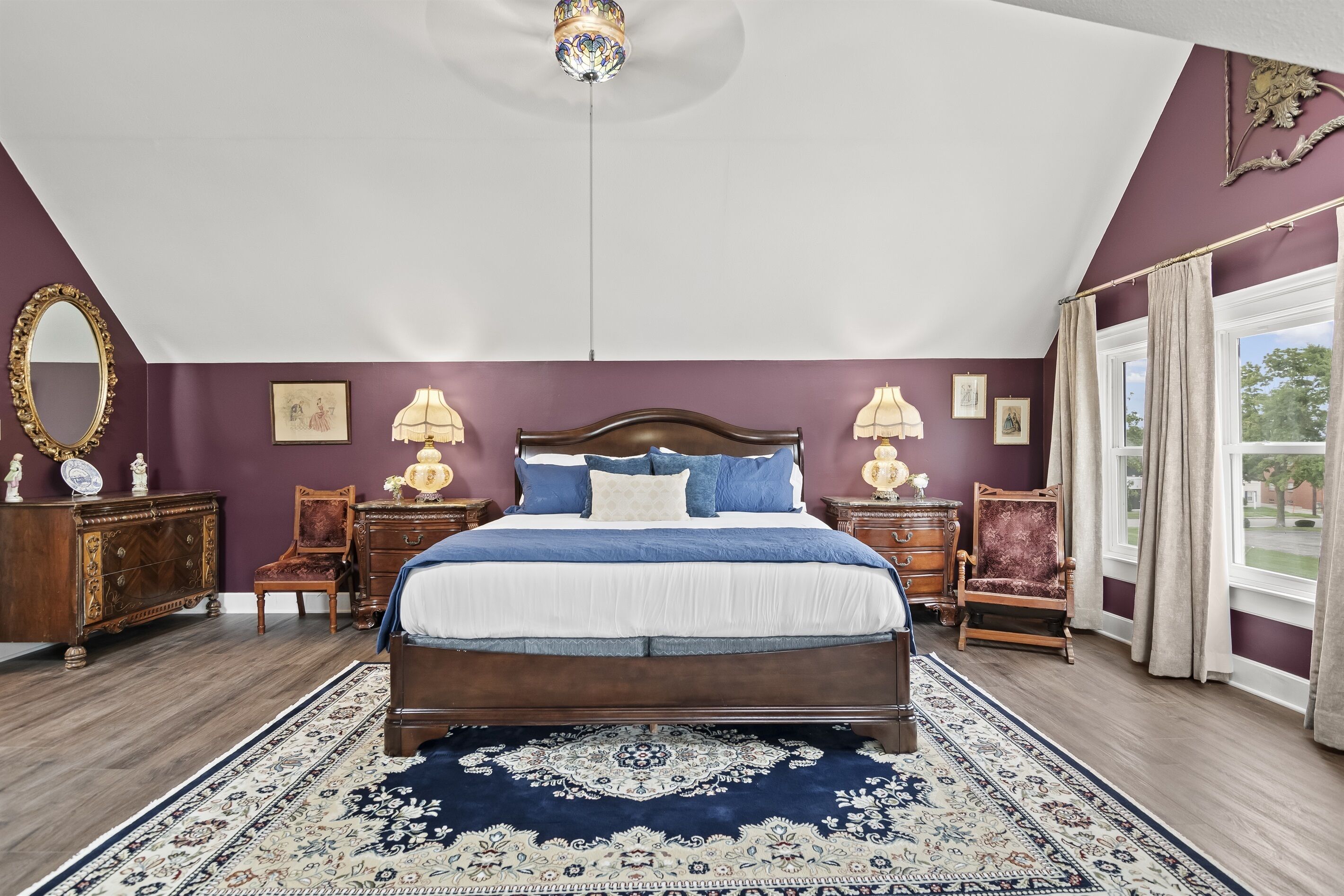 Une chambre à coucher avec un grand lit, un ventilateur de plafond, un lustre et une vue sur l’extérieur par une fenêtre.