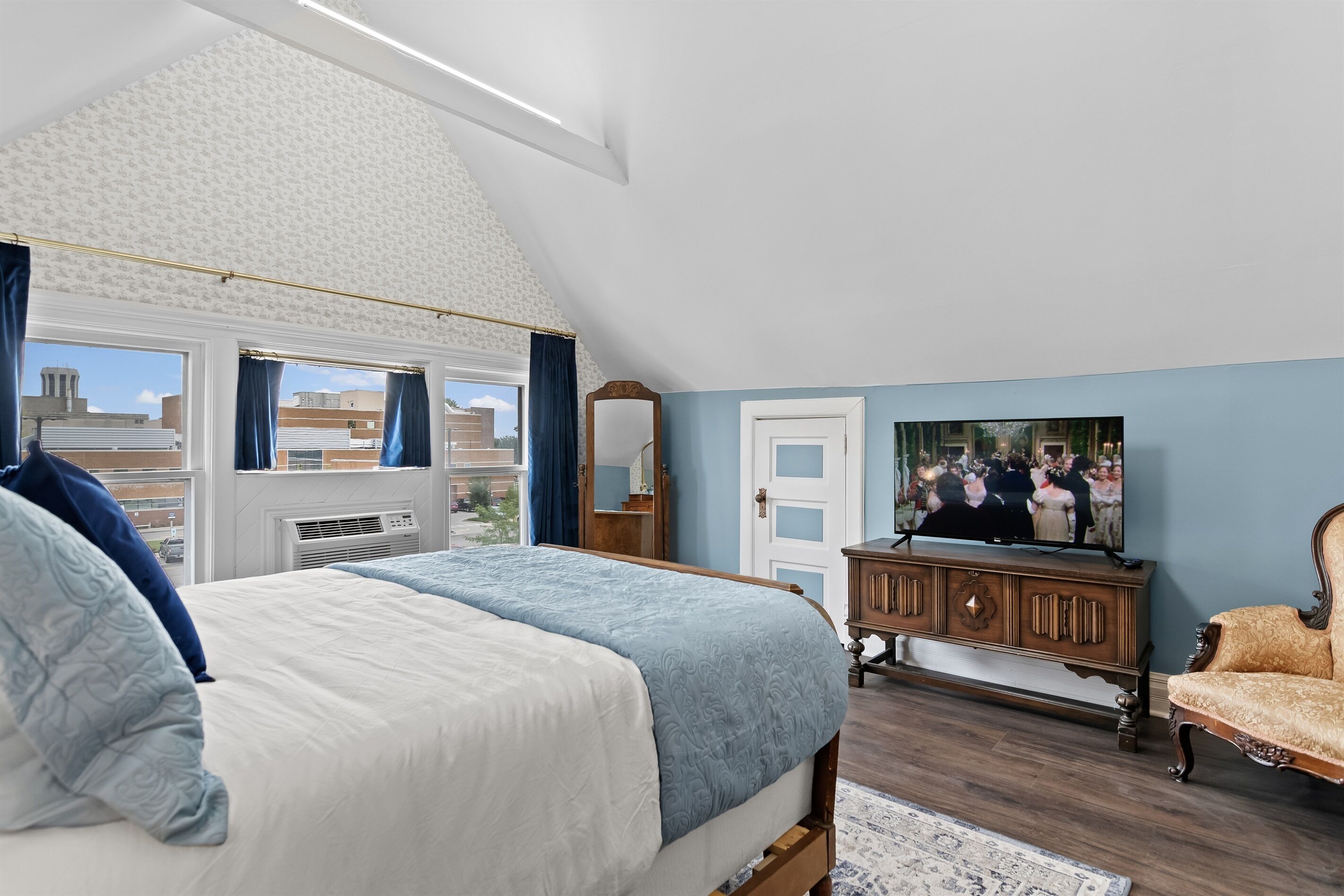 A bedroom with a large bed, a dresser, a television, and a window with curtains.