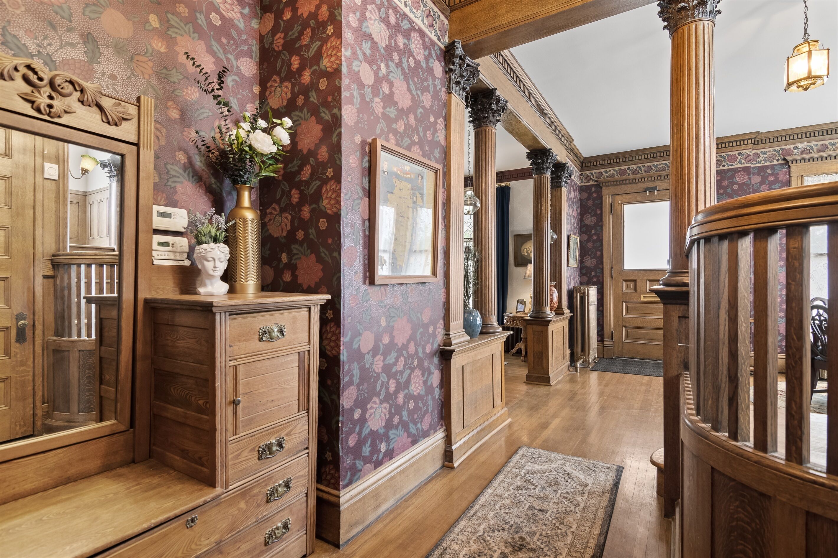 Un vaste hall d’entrée avec des boiseries, un papier peint à motifs floraux et un grand miroir.