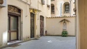 A narrow street with a building featuring a large wooden door, a wrought iron gate, and a small window with a decorative grille.