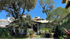 A backyard with a swimming pool, a house with a tiled roof, and various plants. - Casa de Praia com Trilha Privativa em Condomínio Fechado (Florianópolis)