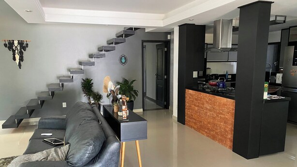 A modern living room with a grey sofa, a coffee table, and a staircase leading to an upper floor. - Casa de Praia com Trilha Privativa em Condomínio Fechado (Florianópolis)