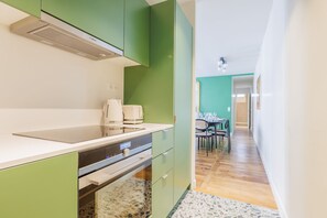 A modern kitchen with green cabinets, a white countertop, and a built-in oven. There is a dining area with a table and chairs visible in the background. - Bright & Stylish Two-Bedroom Apartment with Modern Comforts in Saint-Germain (Paris)
