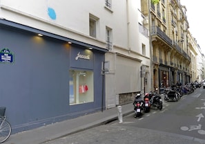 A storefront with a sign reading "Jacadi" and a row of parked motorcycles along the sidewalk. - Bright & Stylish Two-Bedroom Apartment with Modern Comforts in Saint-Germain (Paris)