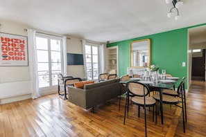 A dining area with a green accent wall, a sofa, and a dining table set for six. - Bright & Stylish Two-Bedroom Apartment with Modern Comforts in Saint-Germain (Paris)