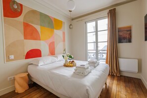 A hotel room with a large bed, a window with curtains, a wall art piece, and a radiator. - Bright & Stylish Two-Bedroom Apartment with Modern Comforts in Saint-Germain (Paris)