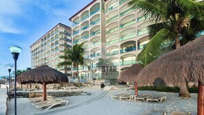 A hotel with multiple balconies, palm trees, and thatched umbrellas.