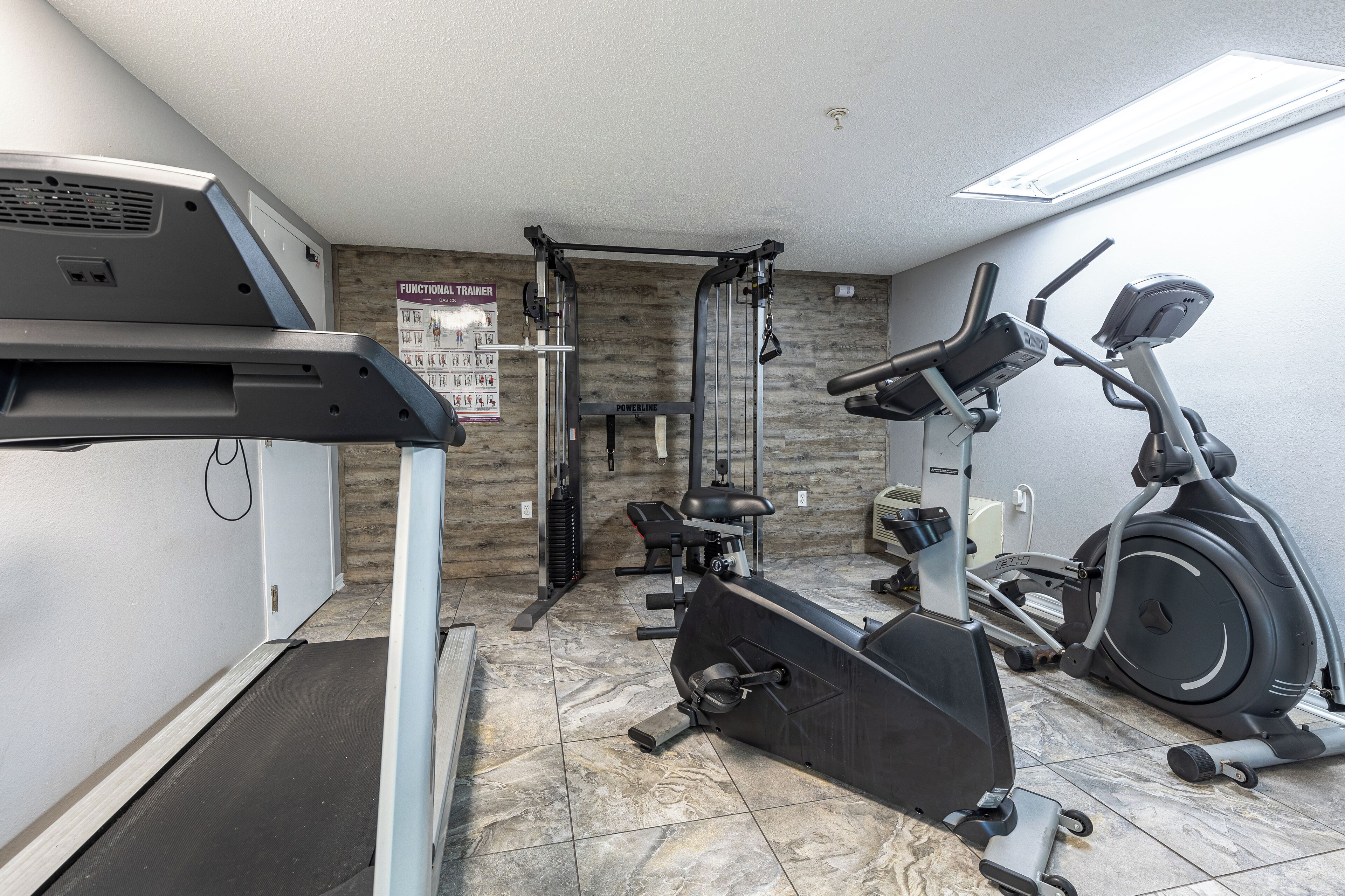 Ein Fitnessstudio mit Laufband, Crosstrainer und Krafttrainingsgeräten.