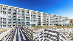 A multi-story hotel with balconies, a boardwalk leading to the beach, and a sign indicating no personal vehicles.