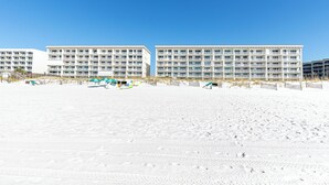 A beachfront hotel with multiple balconies, a sandy beach in front, and a clear blue sky.