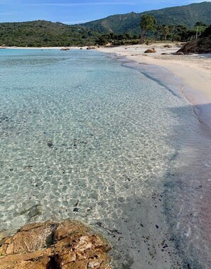 A beach with clear shallow waters, a sandy shore, and a backdrop of hills.