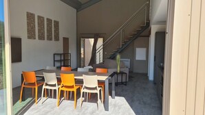 A modern interior with a dining area featuring a wooden table and orange chairs, a staircase, and a view through a glass door. - Zanzimare Casa Petru_T2 (Porticcio)