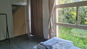 A bedroom with a bed, a window with curtains, a staircase, and a view of greenery outside.