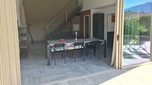Un interior moderno con comedor, escalera y puerta de cristal que da a un patio exterior.