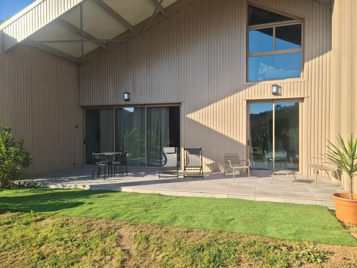 A modern building with a covered patio area, outdoor seating, and a well-maintained lawn.