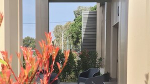 An outdoor seating area with tables and chairs, surrounded by plants and a building structure.