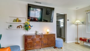 A modern living room with a wooden cabinet, a blue sofa, a small table with a vase of flowers, and a floor lamp. - Albuquerque Retreat w/ Hot Tub - Central Location! (Albuquerque)